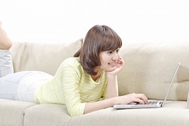 自宅のソファーでリラックスした状態でPCを操作してネット注文している女性の画像